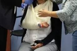 Two people assisting a person wearing a sling on their right arm.
