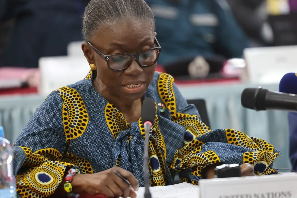 Ms. Anita Kiki Gbeho, Officer in Charge, SRSG and DSRSG-Resident/Humanitarian Coordinator seated at a conference table speaking into a microphone, wearing a patterned blue and yellow outfit, with documents and water bottle on the table.