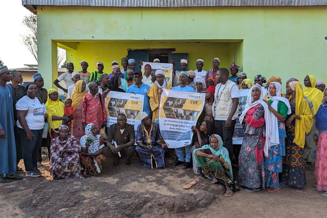 Un groupe de personnes pose pour une photo devant un bâtiment, tenant une banderole