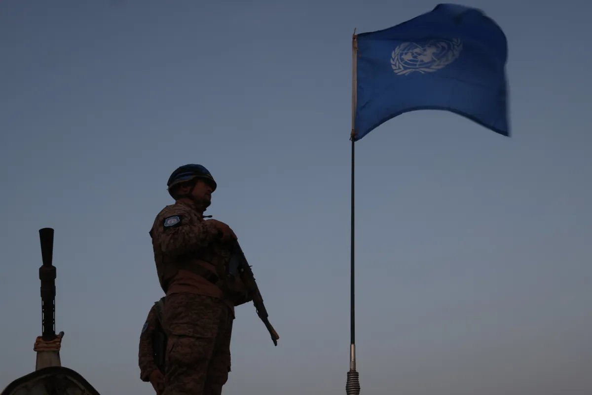A UN peacekeeper standing next to the UN flag