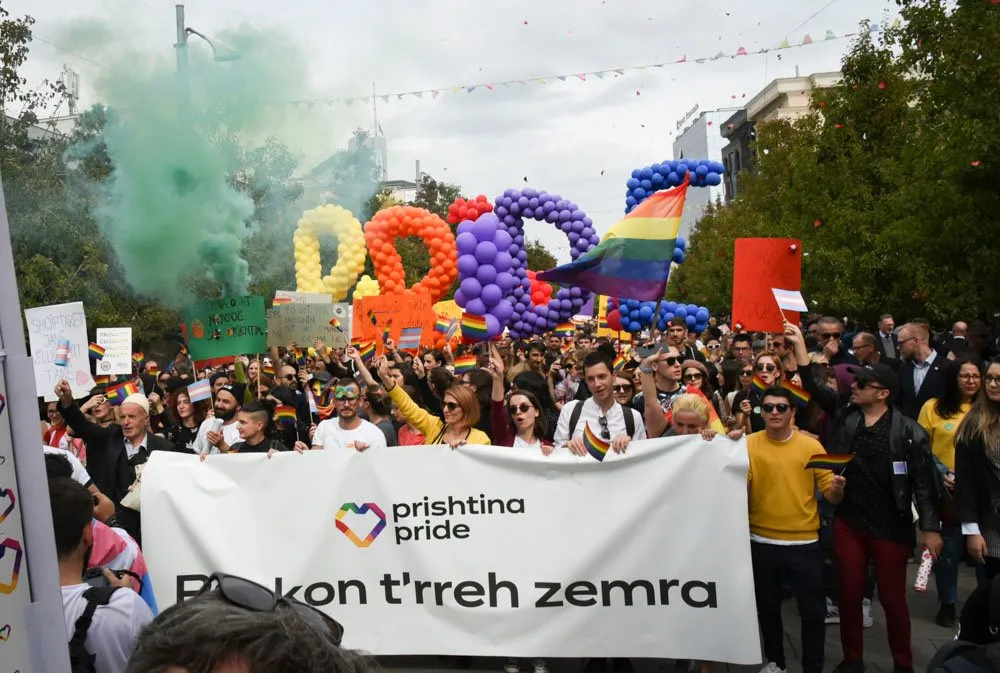 People march in a parade under the word "Pride" made out of balloons